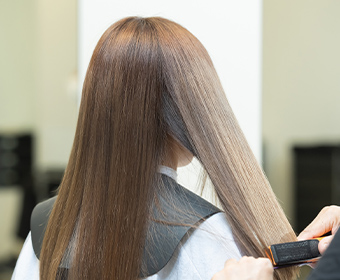 ロングヘアのお客様にストレートアイロンでヘアセットしているヘアサロンの様子